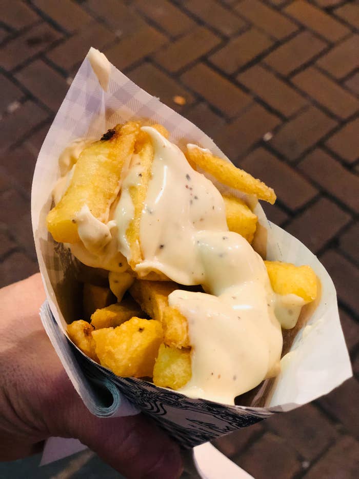Fries covered in mayo in a paper cone.