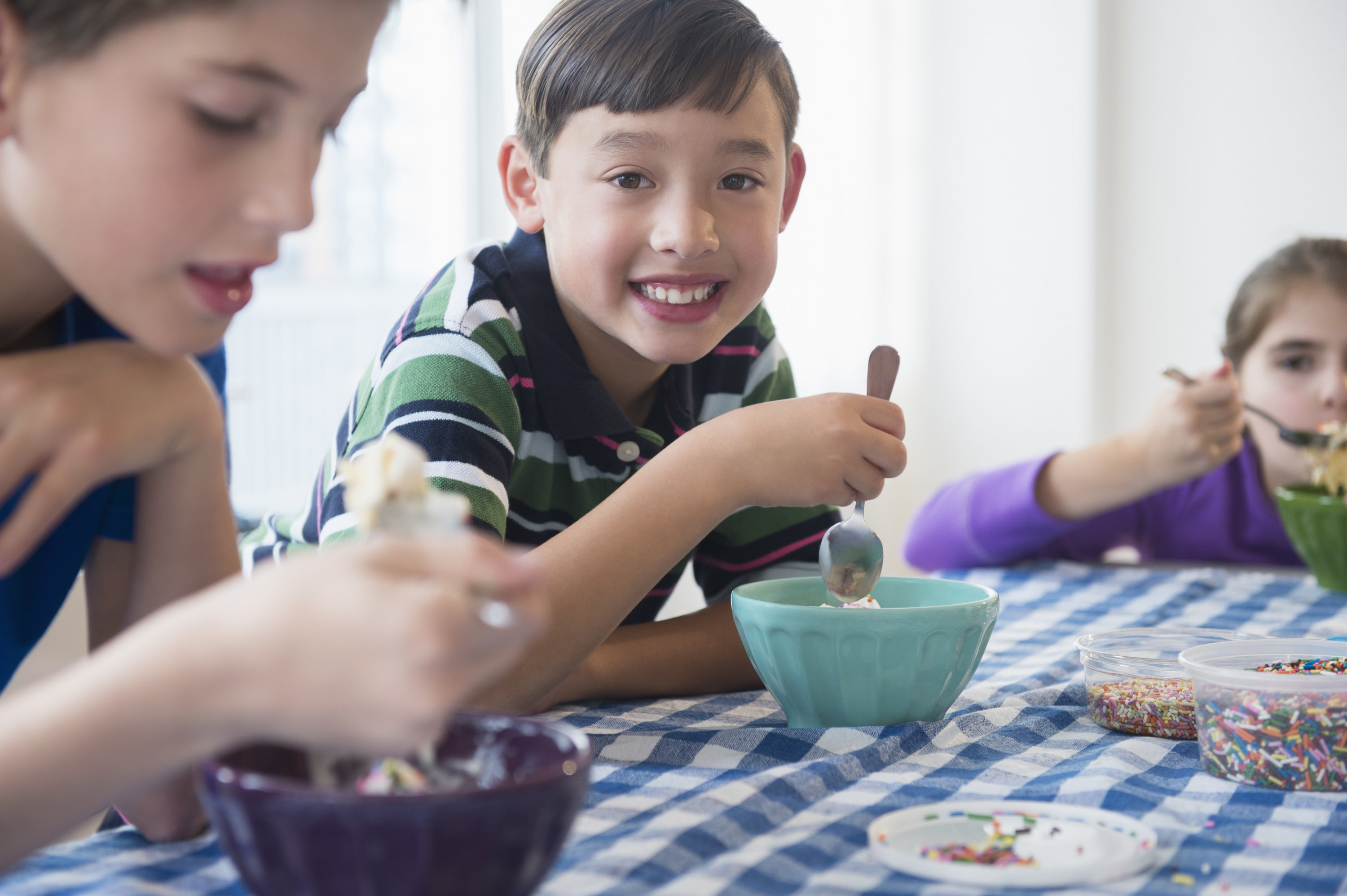 A boy happily looks on as he digs into his ice cream sundae.