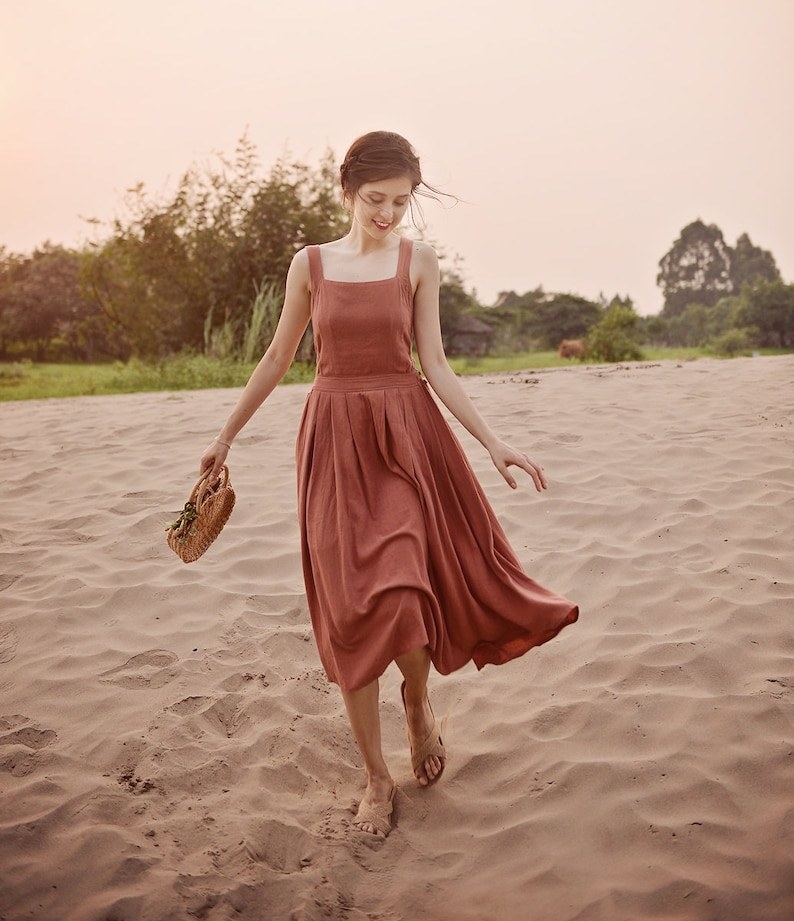 Model is walking on sand wearing a dusty rose colored dress