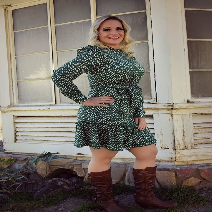 A customer review photo of them wearing the tie-waist long-sleeve dress in green printed with little white daisies