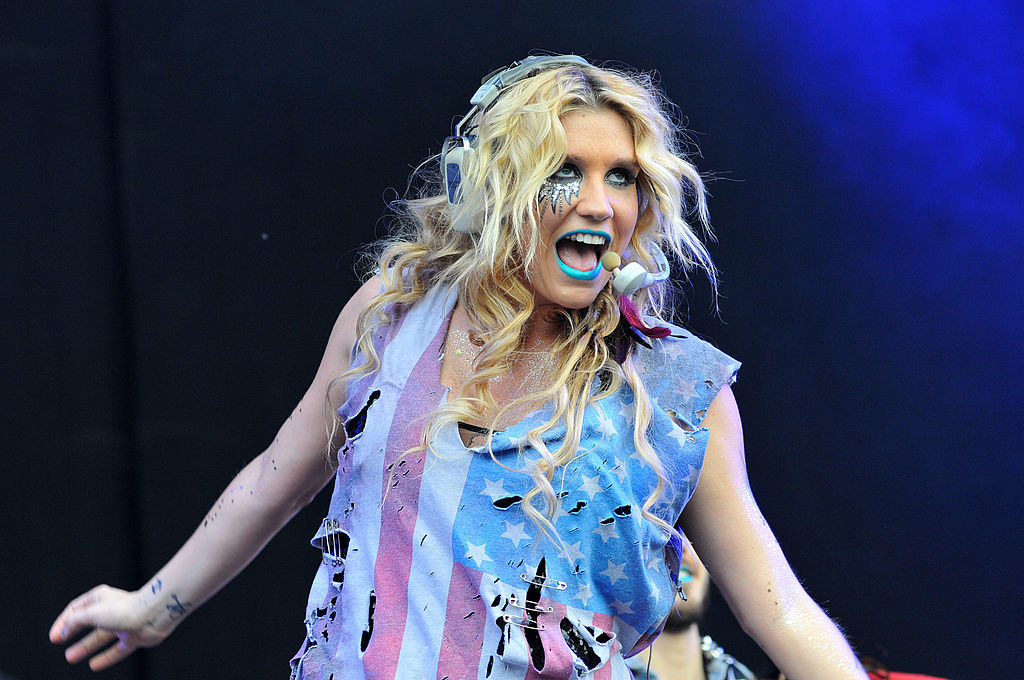 Kesha performing on stage in a torn-up American flag tank top