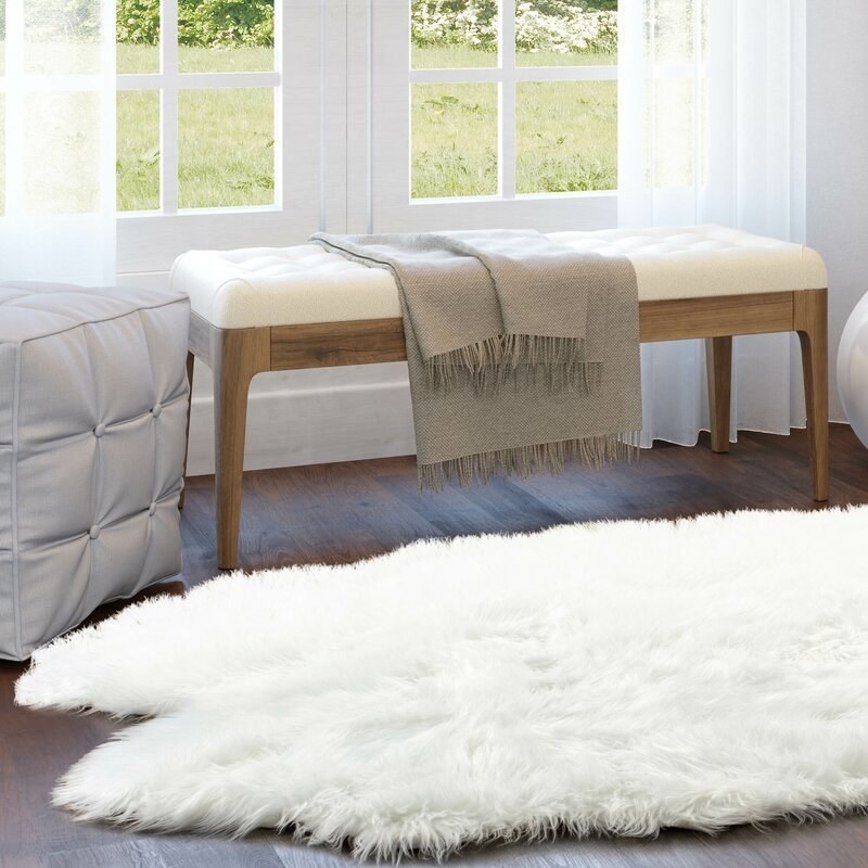 White faux sheepskin rug next to a bench and pouf.