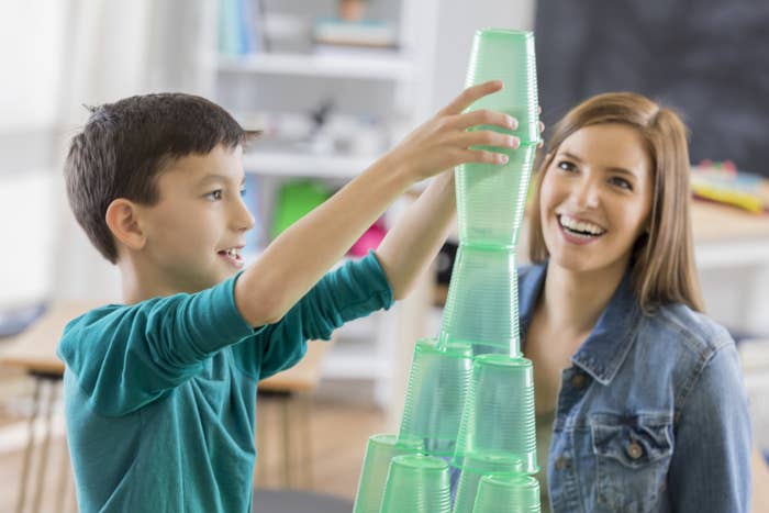 A boy stacks clear cups while his mom watches