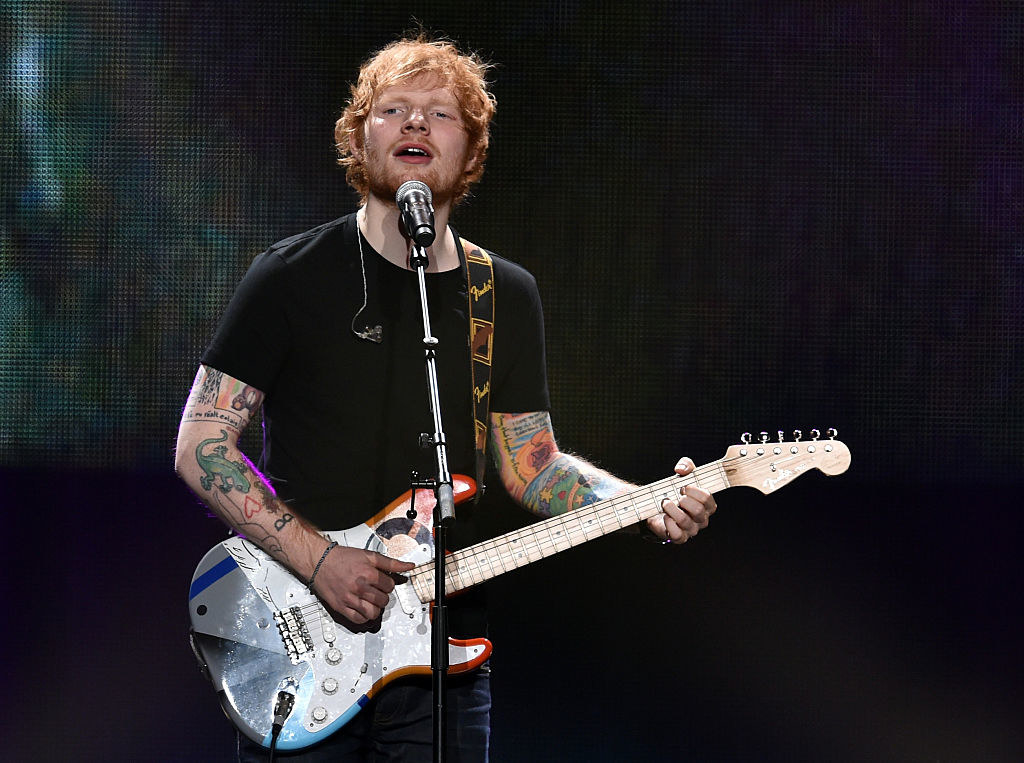 Ed Sheeran plays guitar on stage for an iHeartMusic concert