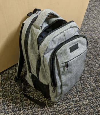 Reviewer image of gray backpack upright on floor showing multiple front pockets, laptop sleeve, and storage 