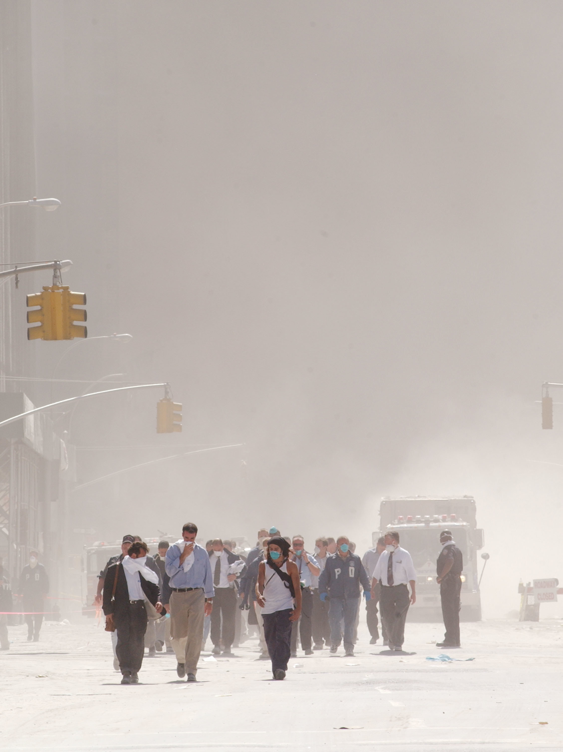 People wearing masks and covering their faces walk through a street that is all white from ash 