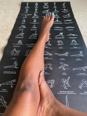 reviewer sits on black yoga mat with pose pictures