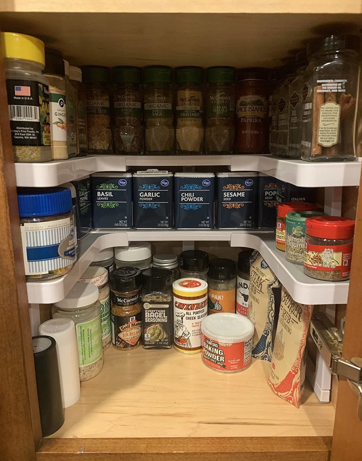 a reviewer photo of spice bottles on the expandable shelves in a kitchen cabinet 
