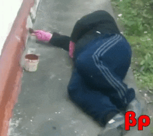 A man lays on the ground lazily painting a curb