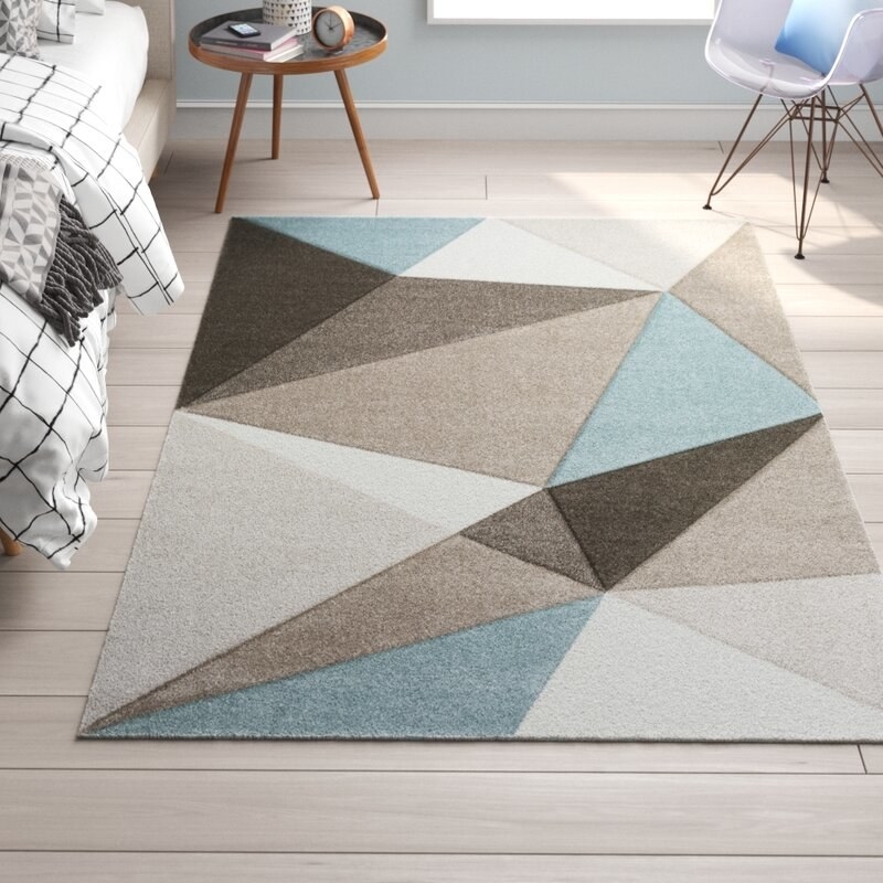 Geometric rug made up of blue, beige and brown triangles, placed on hardwood floors in a bedroom.