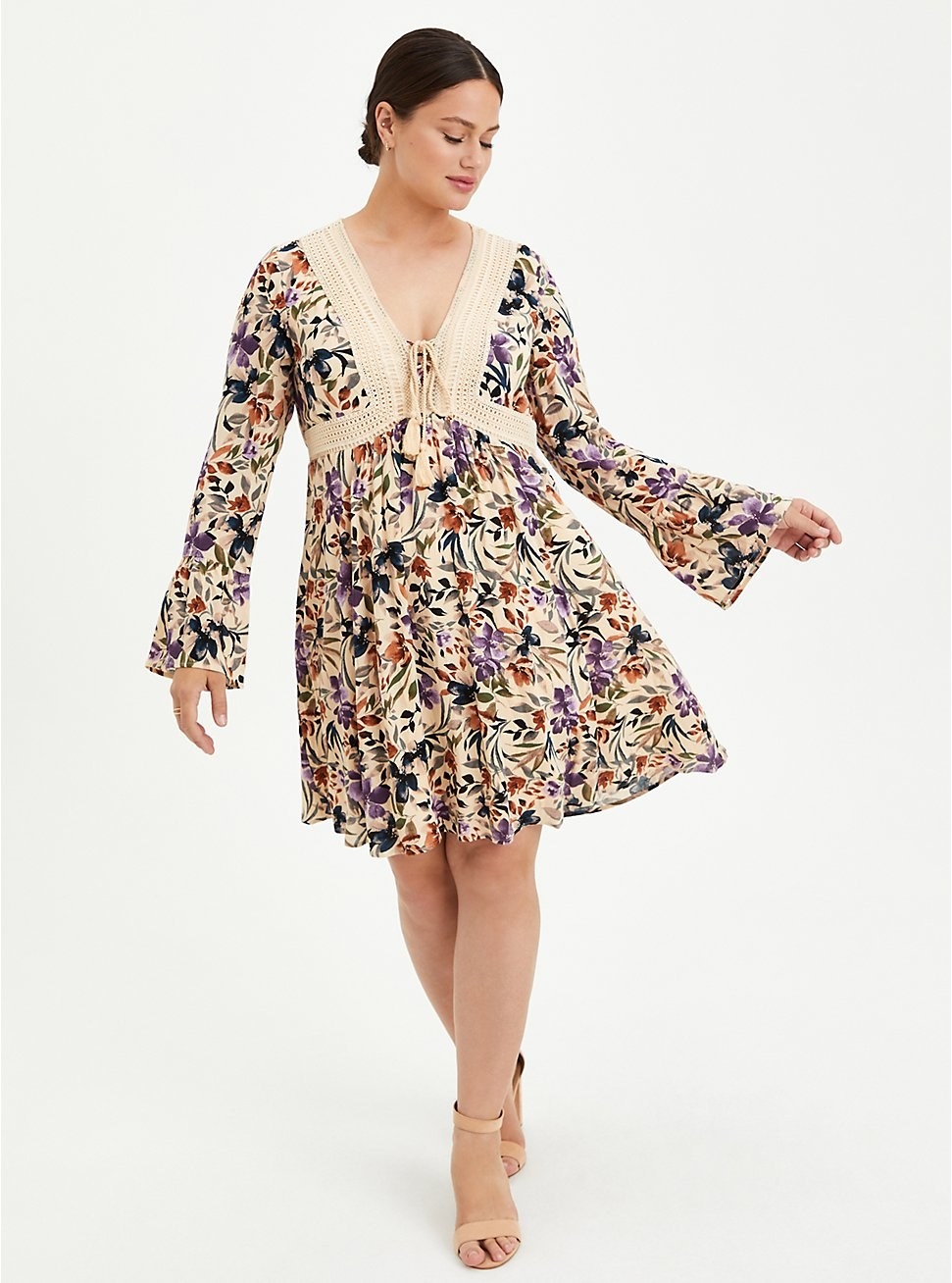 model in tan bell sleeve short dress with colorful floral print and crochet trim and tie at the bust