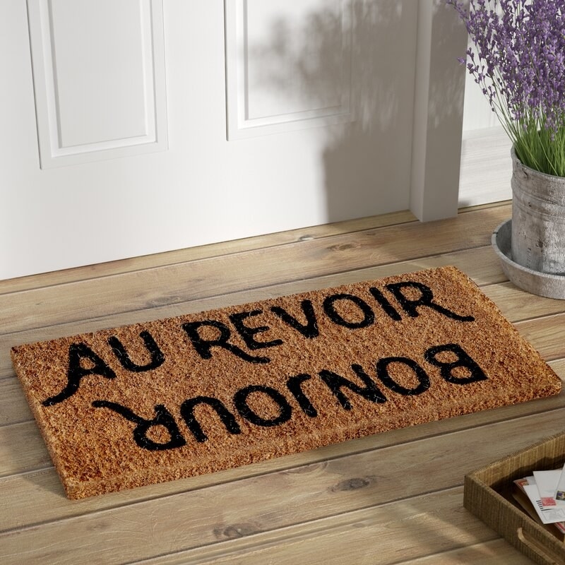 Natural colored door mat with the words &quot;Bonjour&quot; and &quot;Au revoir&quot; printed on it in black.