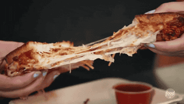 Two hands slowly pull apart a spaghetti and grilled cheese sandwich