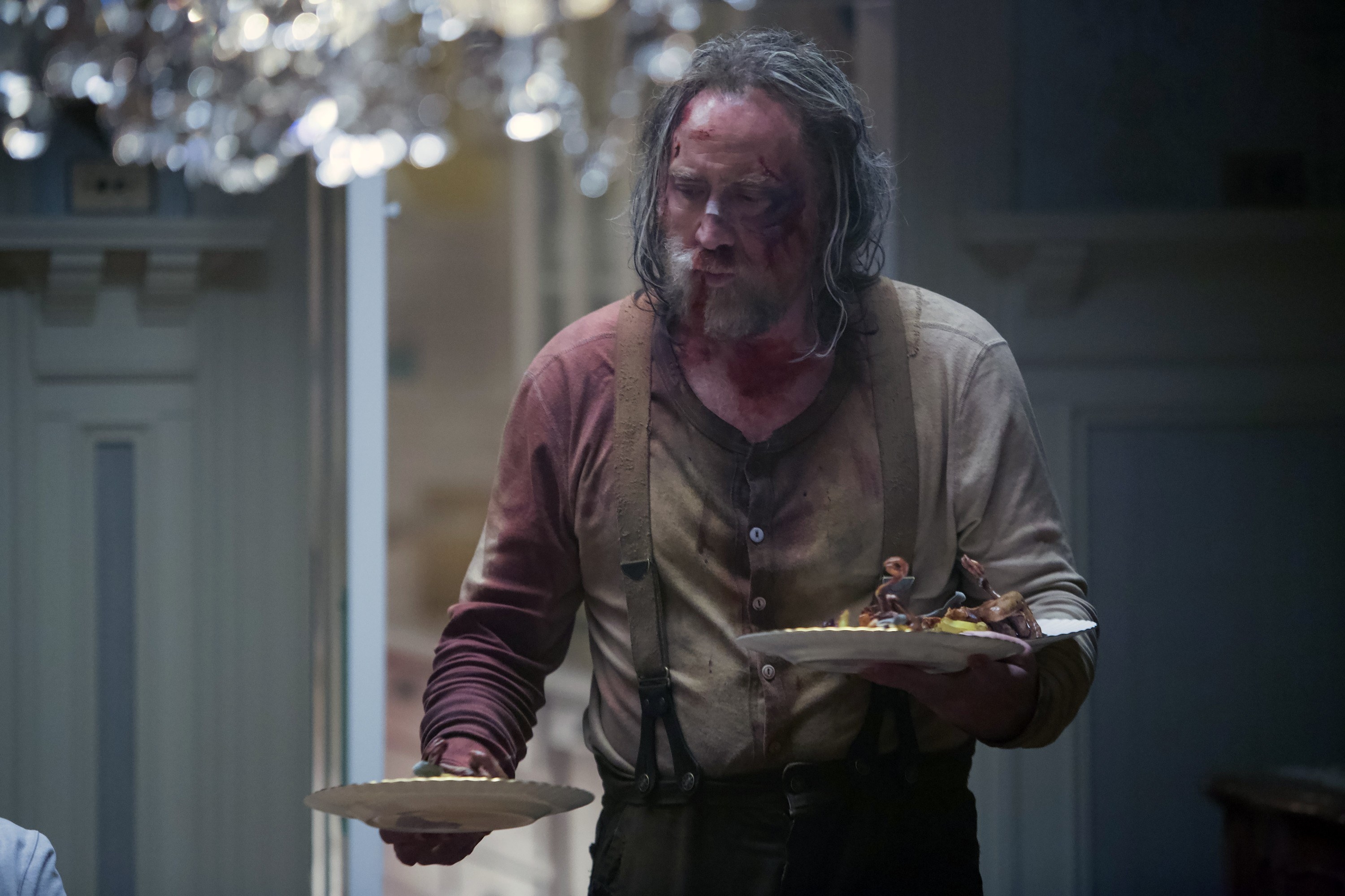 A bloodied Nicolas Cage holds two plates