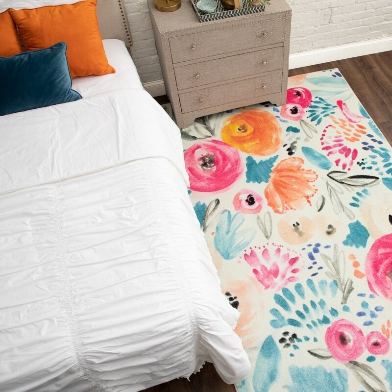 Colorful floral rug next to a bed and nightstand in a bedroom.