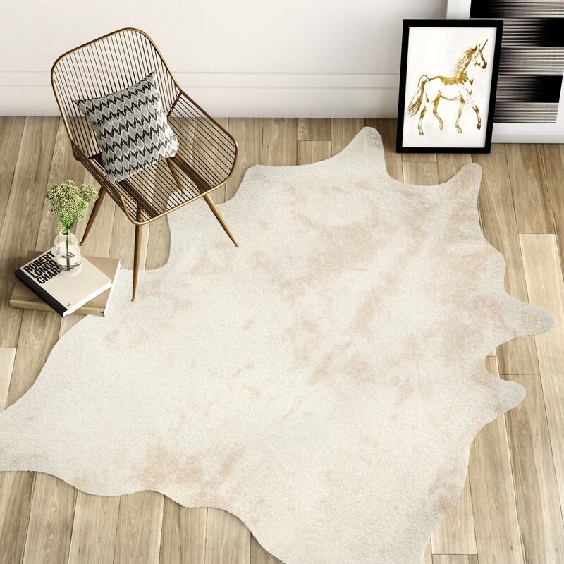 Neutral cowhide rug on hardwood floors with chair, books and artwork next to it.