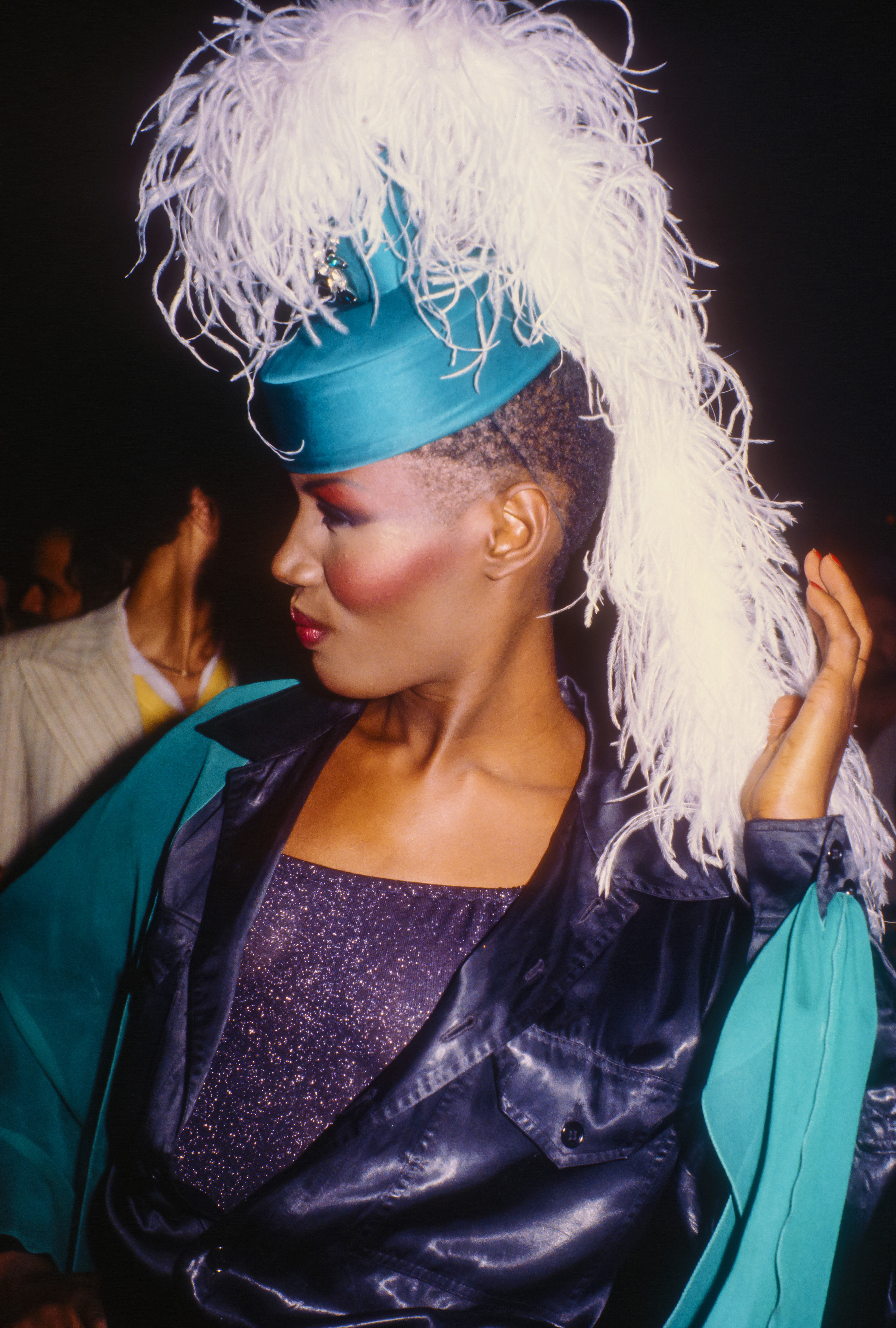Photo of Grace Jones in bright blush and a feather adorned hat