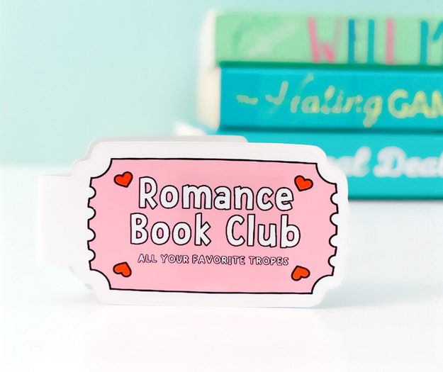 A white magnetic bookmark with a pink graphic shaped like a ticket that says &quot;Romance Book Club, All Your Favorite Tropes&quot;