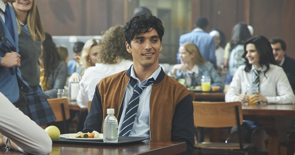 Taylor as Marco wearing a school uniform and sitting in a cafeteria, surrounded by other students. He has a plate of food and water in front of him