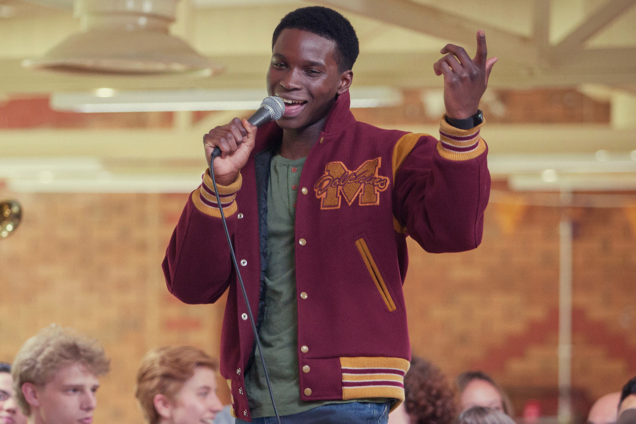 Kedar as Jackson, clad in a jacket, holding a mic and singing