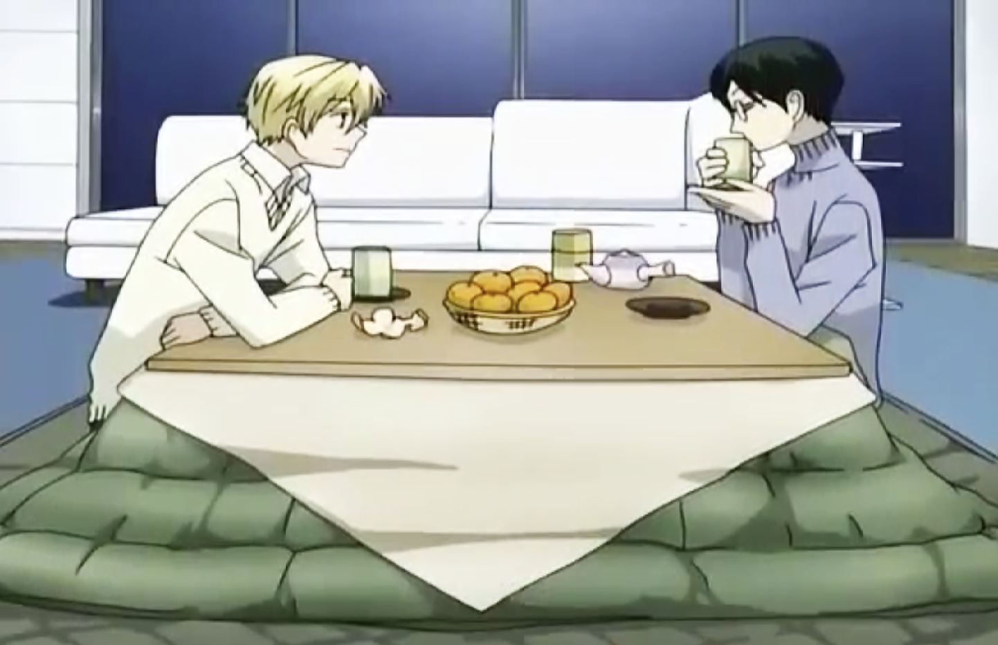 Two anime characters sitting at a low dining table drinking green tea; the table is covered by a kotatsu