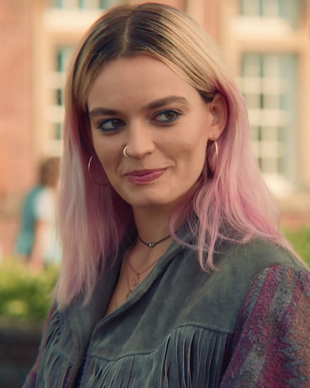 Emma as Maeve wearing a ruffle jacket and smiling sideways