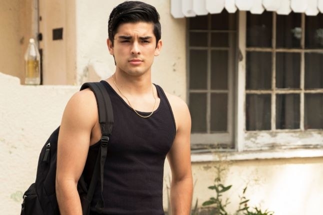 Tinoco as Cesar in a vest with a bag hanging on his right shoulder