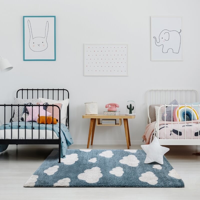 Blue rug with white clouds shown in a kids&#x27; room with two twin beds and a nightstand in between them.