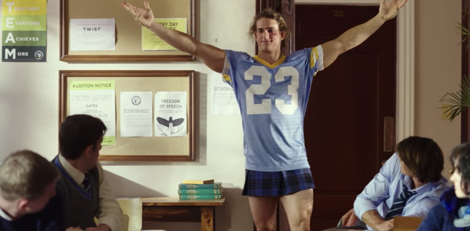 From &quot;The Kissing Booth&quot; image shows a teenaged boy in a jersey, wearing a plaid mini skirt and smiling.