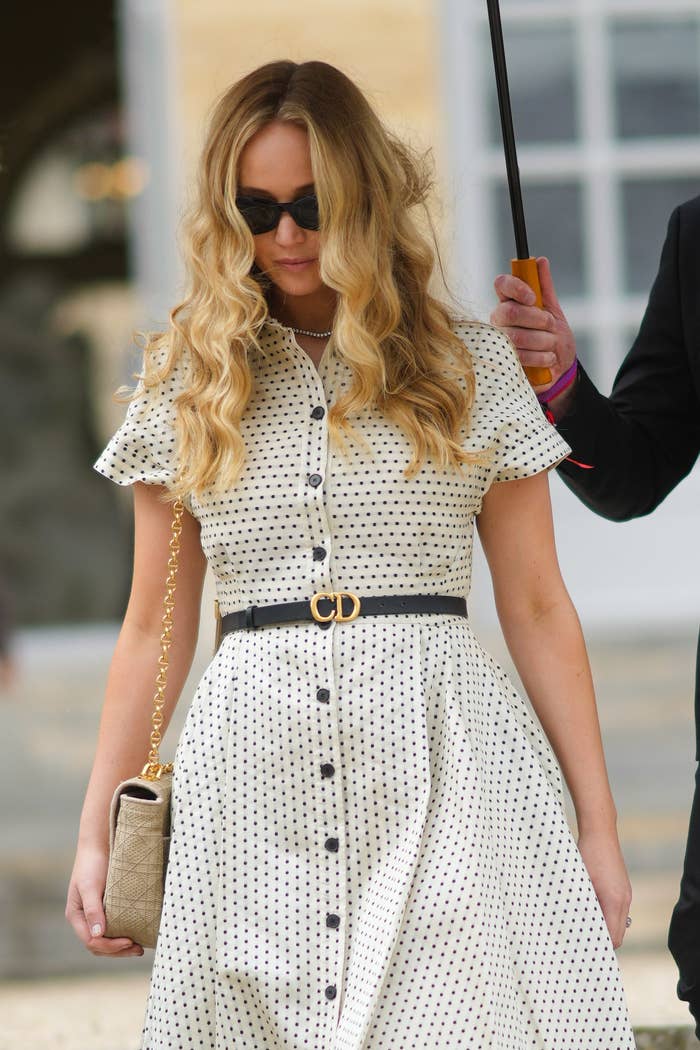 Jennifer Lawrence walks down stairs while wearing a polka-dot dress with a clutch at her side