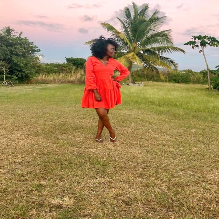 reviewer wearing the dress in red on a grassy field with a palm tree in the back