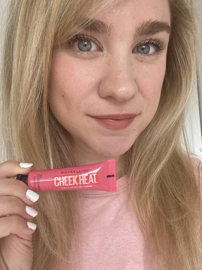 BuzzFeed writer holding pink tube of Cheek Heat with it applied to cheeks