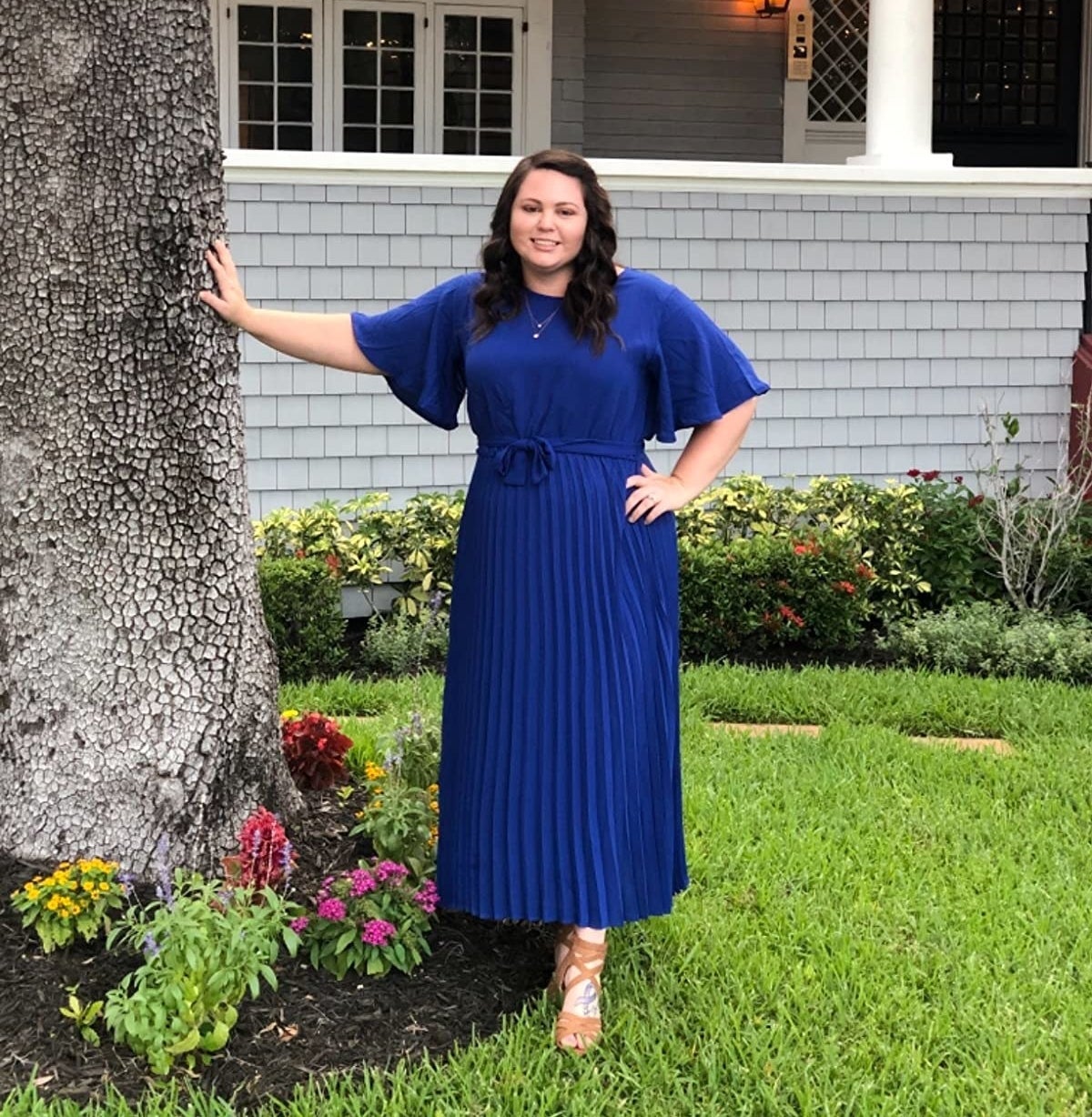 reviewer wearing the dress in blue leaning against a tree