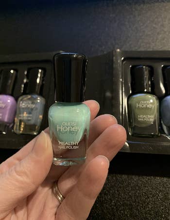 Reviewer holding up small bottle of blue polish with other colors in packaging 