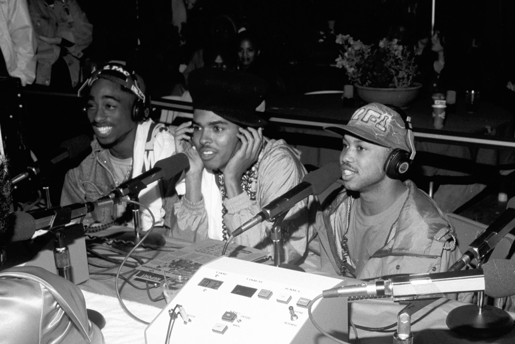 Three men smile and lean forward to talk into microphones