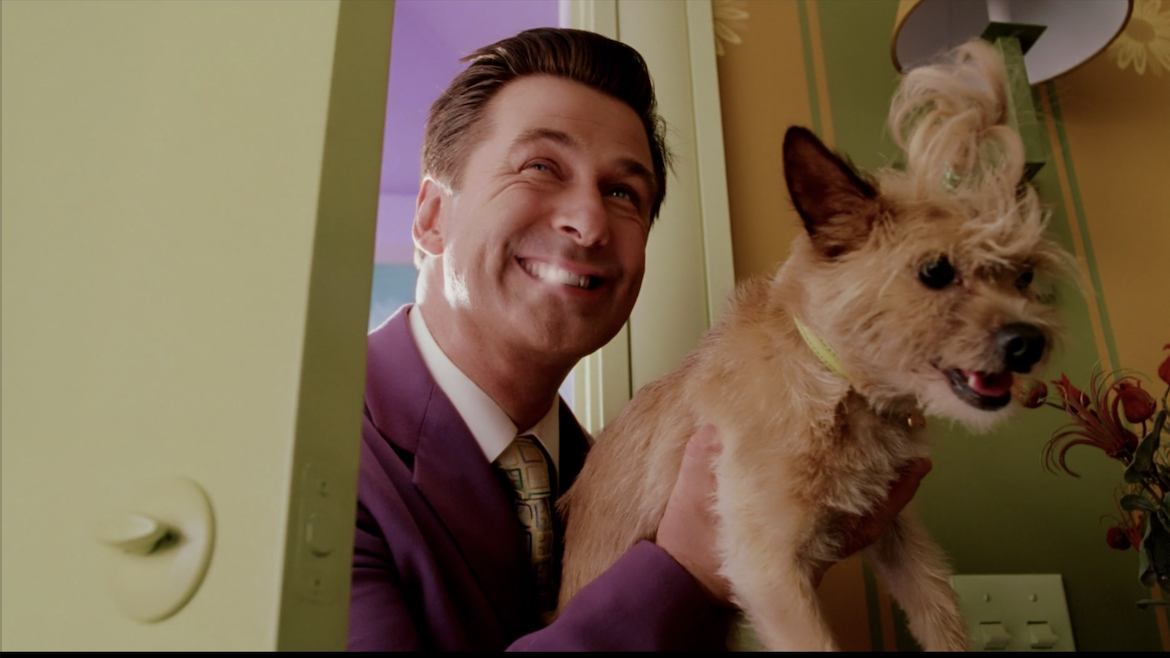 Alec Baldwin, holding the dog, with his teeth glinting