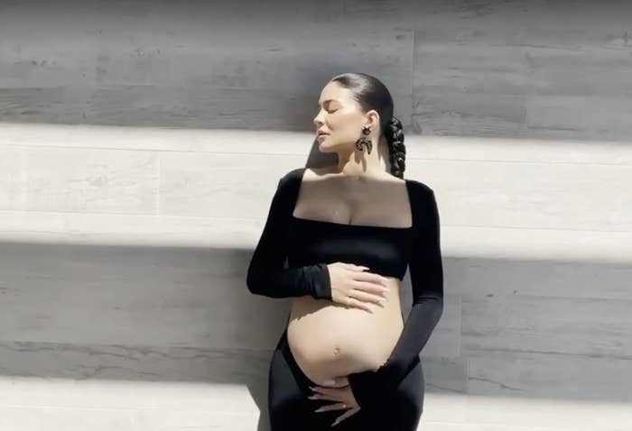 Kylie posing with her hands over her exposed baby bump