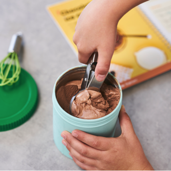 A hand scooping out chocolate ice cream from a teal container