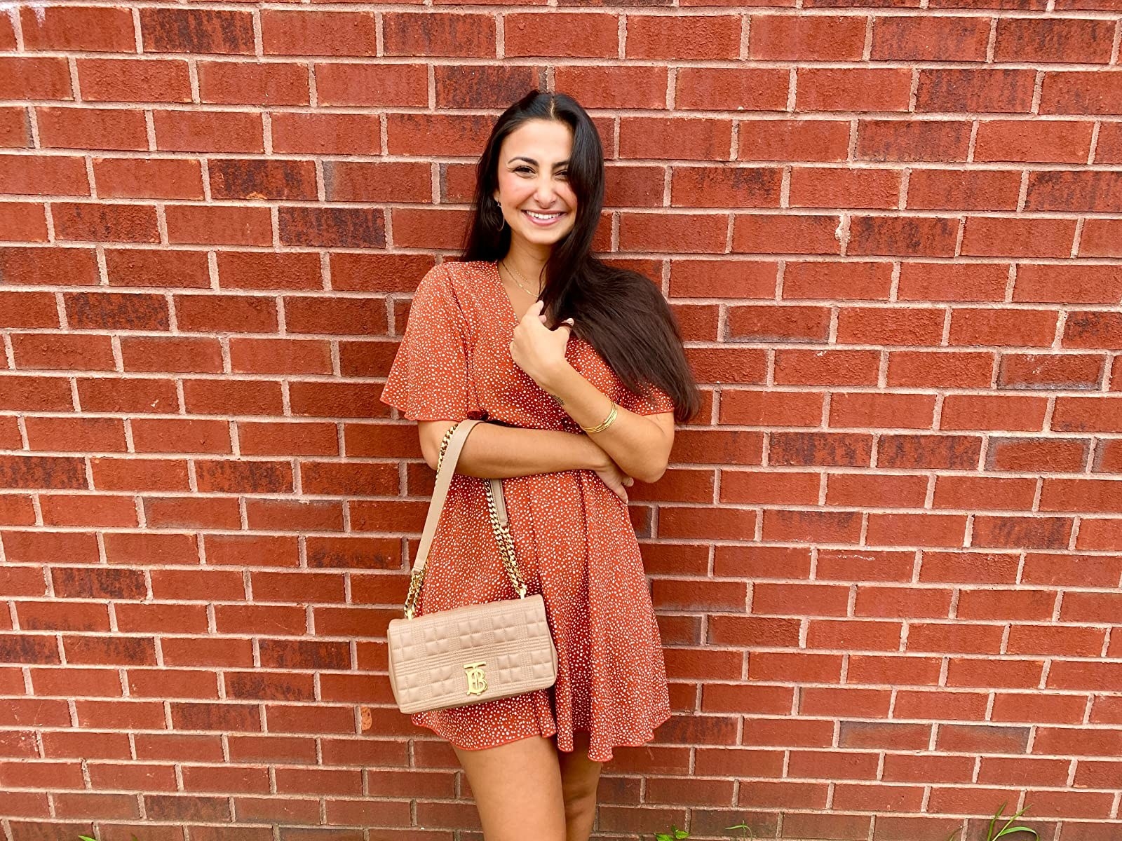 reviewer wearing the dress in red in front of a brick wall carrying a pink purse