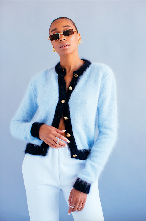 model in square-shaped brown sunglasses and a fluffy blue cardigan and white pants