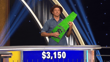 Jason Mraz pretends to play guitar using a Wheel of Fortune wedge. Pat Sajak says, &quot;Don&#x27;t play our wedge.&quot;