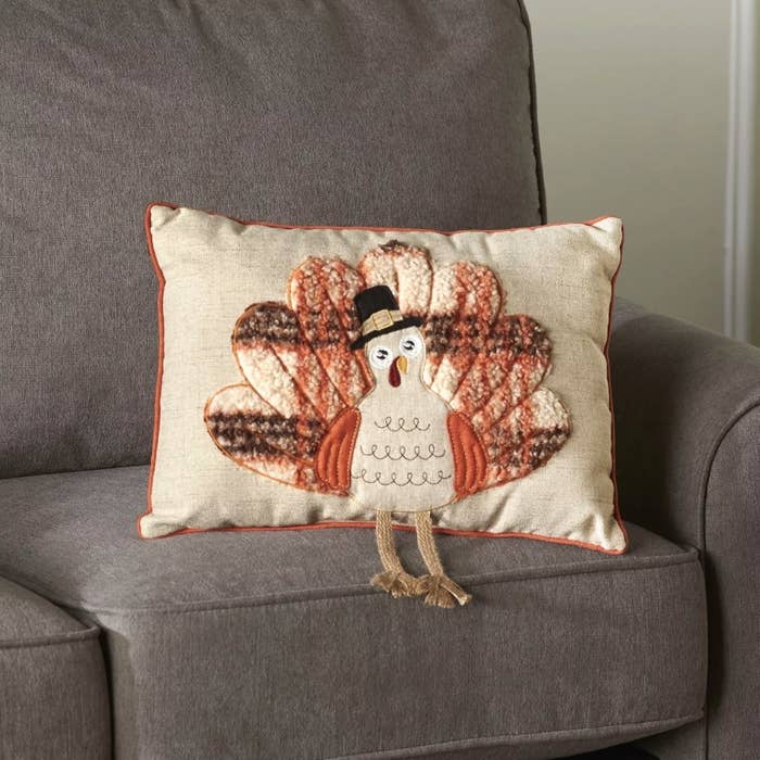 A beige/orange throw pillow with a turkey motif on a couch