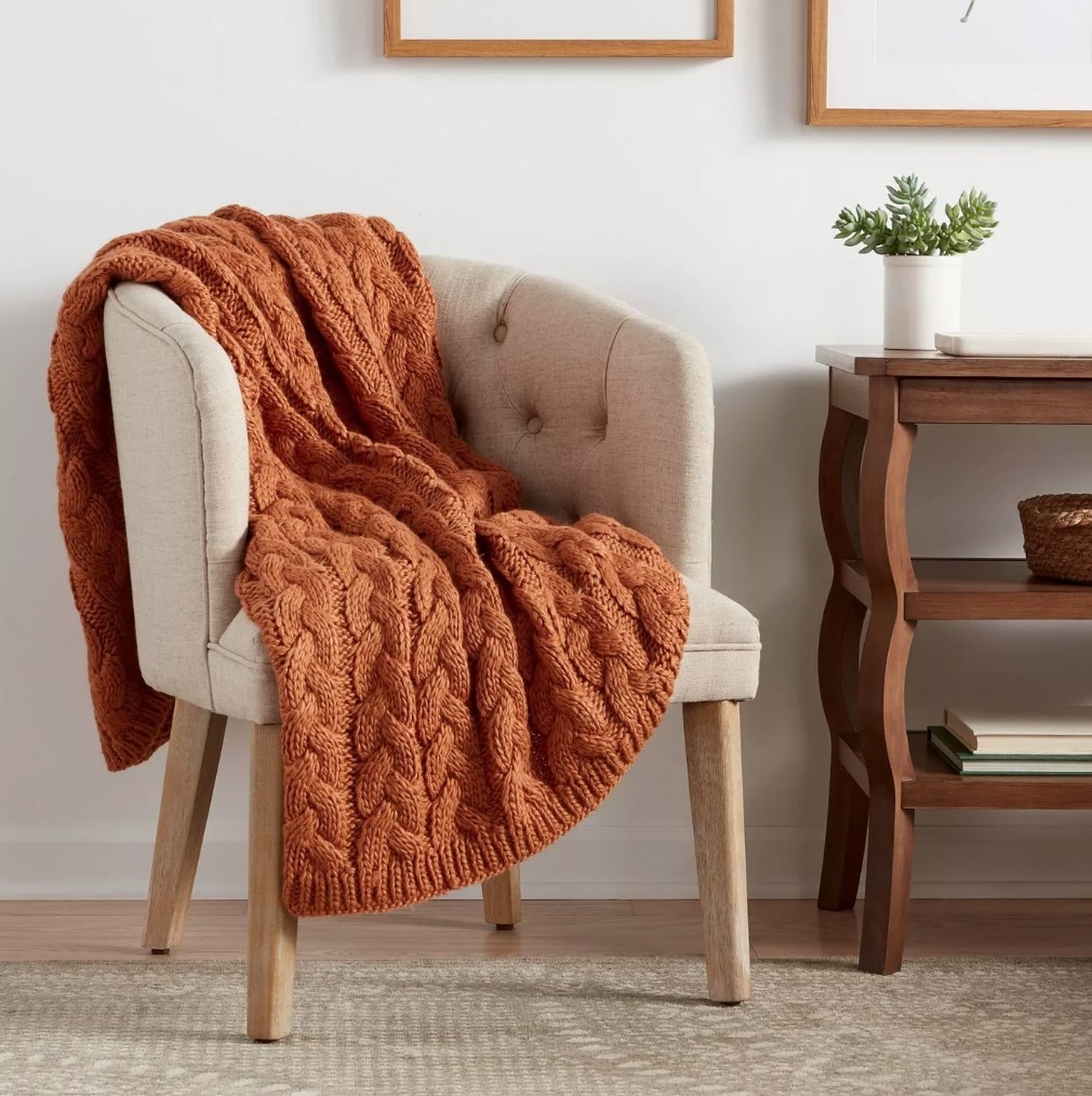A bronze, chunky, cable knit throw blanket draped over an accent chair
