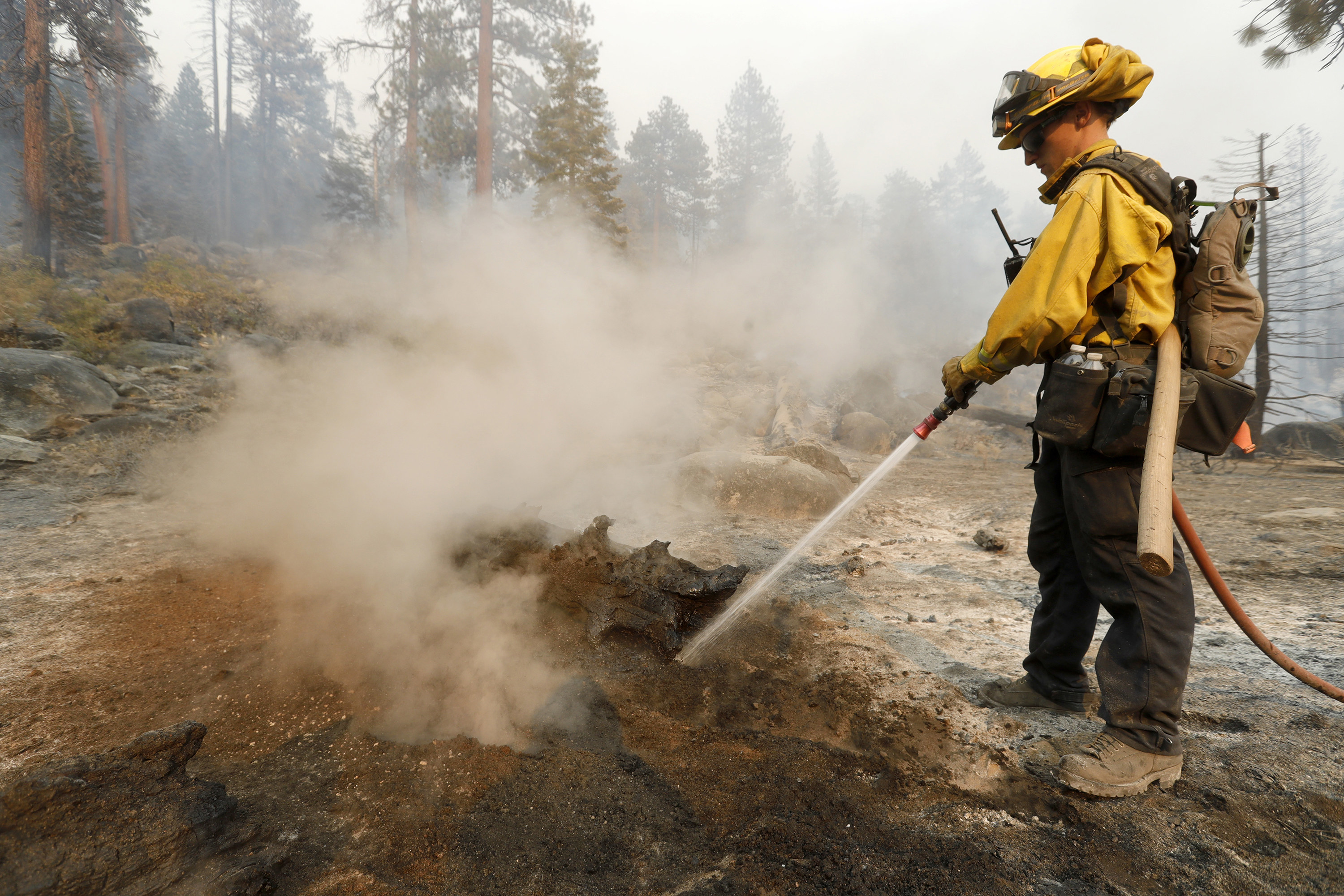 A firefighter points a hose at the ground, where smoke arises from smoldering patches