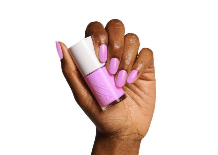 A manicured hand holding a bottle of bright pink nail polish