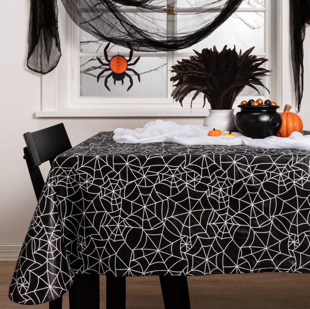 A black/white, spiderweb tablecloth atop a table in a dining room filled with halloween decor