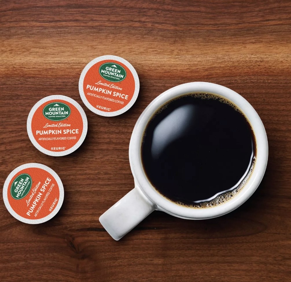 3 Green Mountain pumpkin spice K-Cup pods on a counter next to a cup of coffee