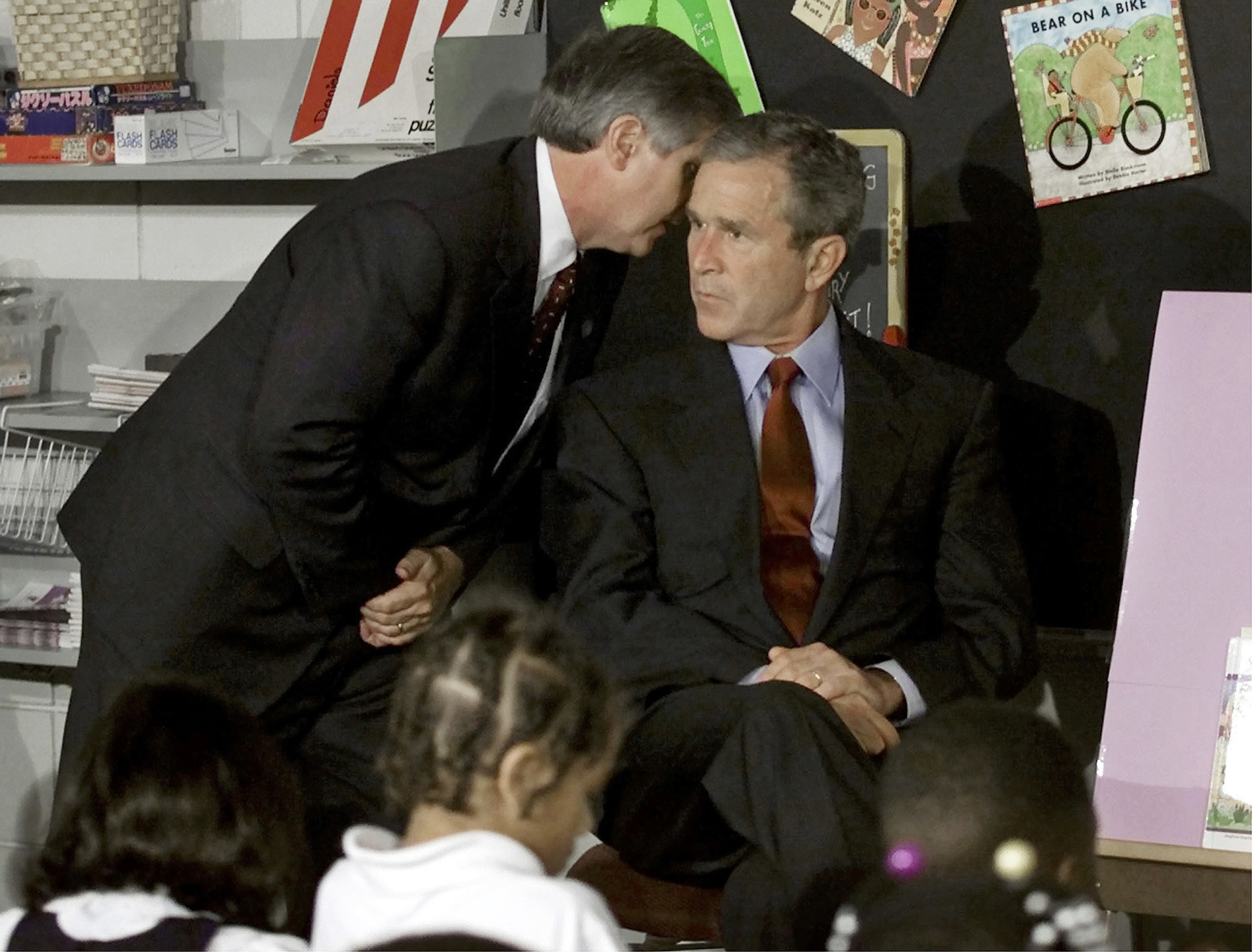 President George W. Bush looking very serious while another man in a suit whispers in his ear in a children&#x27;s classroom