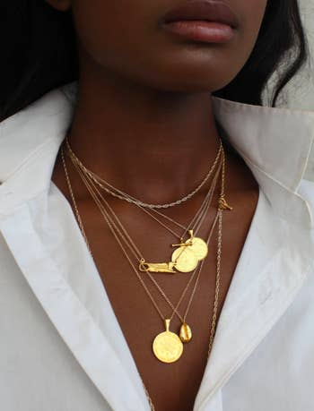 model wearing several coin necklaces which have a flat circular charm like a coin and a skinny gold chain