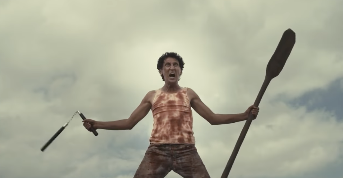 A screaming man wearing a blood-soaked tank top holding nunchucks and a boat paddle